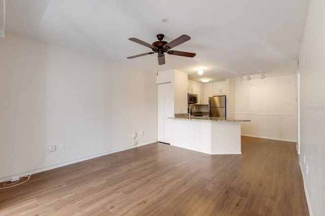unfurnished living room with a sink, ceiling fan, wood finished floors, track lighting, and baseboards
