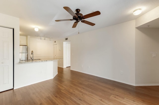 unfurnished living room with ceiling fan, wood finished floors, baseboards, and rail lighting
