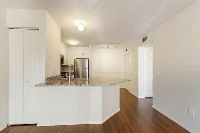 kitchen with stainless steel appliances, a peninsula, light stone counters, dark wood-style flooring, and rail lighting