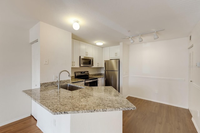 kitchen with stainless steel appliances, a sink, light stone countertops, a peninsula, and track lighting