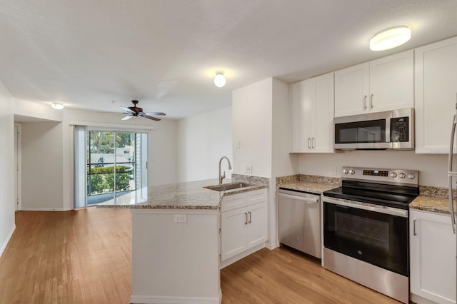 kitchen with appliances with stainless steel finishes, a sink, a peninsula, light wood-type flooring, and ceiling fan