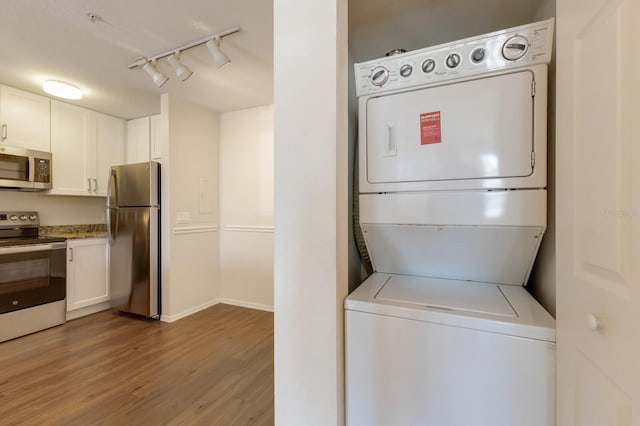 laundry area with stacked washer and clothes dryer, track lighting, wood finished floors, and baseboards