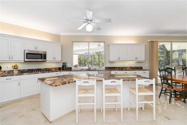 2067 Tocobaga Ln, Nokomis, FL 34275 - kitchen with stainless steel microwave, gas stovetop, ornamental molding, dark stone counters, and white cabinets