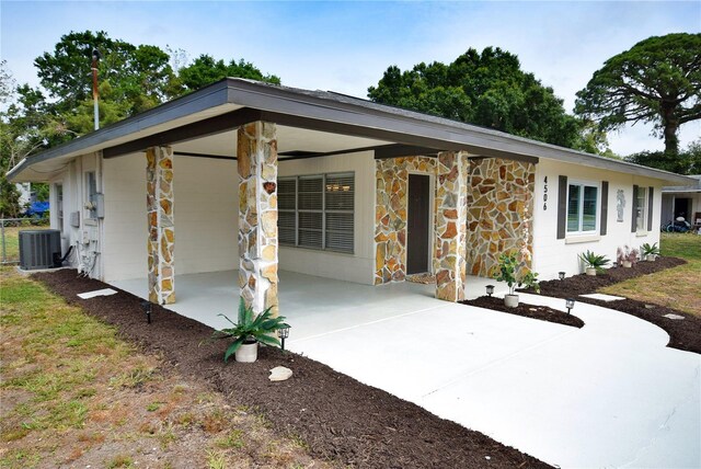 view of front facade with concrete driveway, stone siding, cooling unit, an attached carport, and a patio area