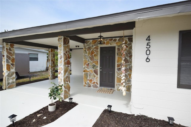 view of exterior entry featuring stone siding and covered porch