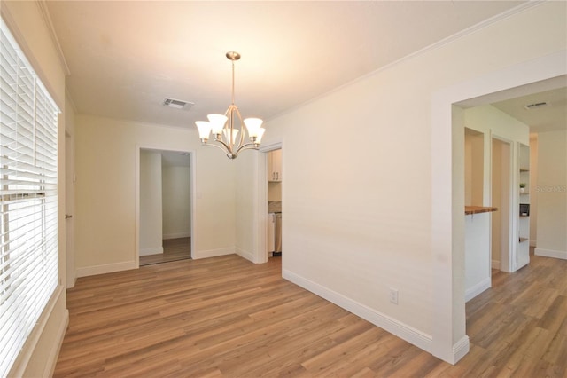 spare room featuring light wood-type flooring, a chandelier, baseboards, and ornamental molding