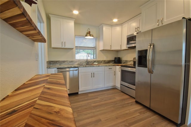 kitchen featuring appliances with stainless steel finishes, a sink, white cabinets, light wood-style floors, and recessed lighting