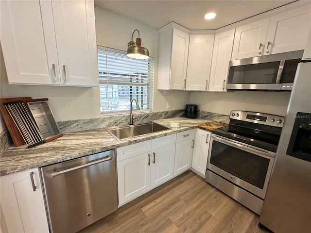 kitchen with appliances with stainless steel finishes, a sink, light wood-style flooring, white cabinets, and recessed lighting