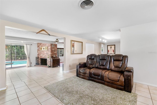 living room with light tile patterned floors, a ceiling fan, a brick fireplace, track lighting, and baseboards
