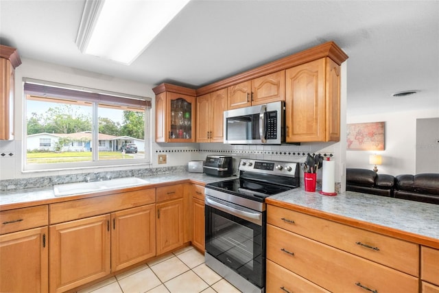 kitchen with stainless steel appliances, a sink, light countertops, glass insert cabinets, and light tile patterned floors