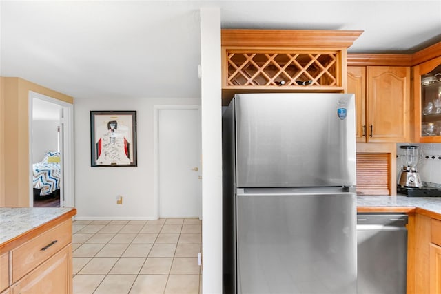 kitchen with appliances with stainless steel finishes, light countertops, light tile patterned flooring, glass insert cabinets, and light brown cabinetry