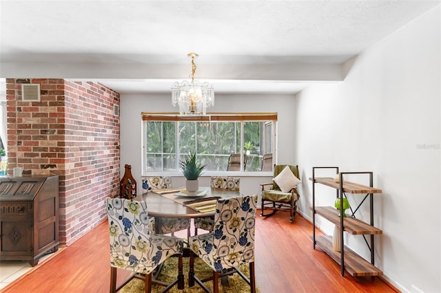 dining area featuring light wood-style flooring, a chandelier, brick wall, and baseboards