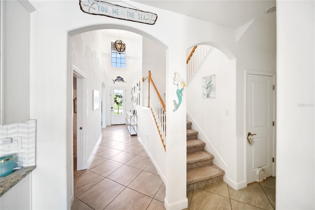 foyer featuring light tile patterned floors, stairs, arched walkways, baseboards, and a high ceiling