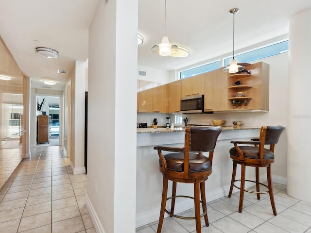 6512 Midnight Pass Rd Unit 303, Sarasota, FL 34242 - kitchen with stainless steel microwave, light tile patterned floors, a kitchen breakfast bar, light brown cabinets, and open shelves