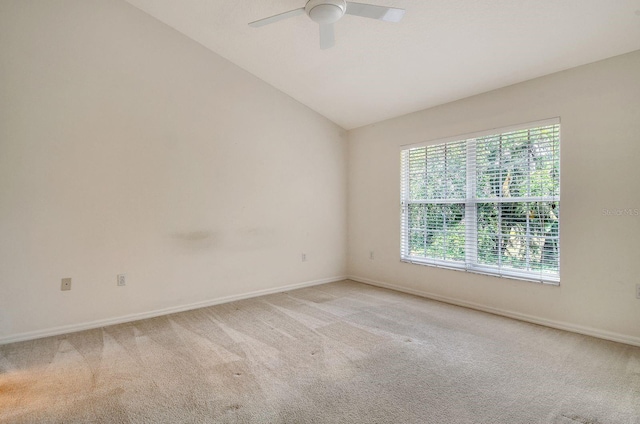 empty room with light colored carpet, a ceiling fan, vaulted ceiling, and baseboards
