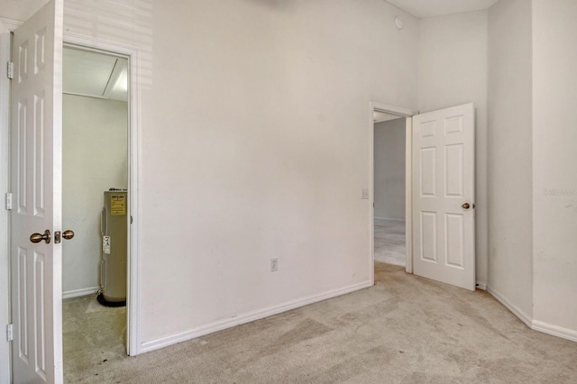 unfurnished bedroom with electric water heater, light colored carpet, and baseboards