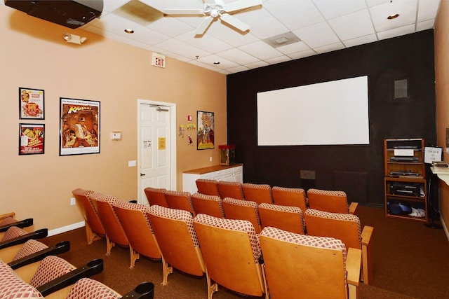 carpeted home theater room featuring ceiling fan, a drop ceiling, and baseboards