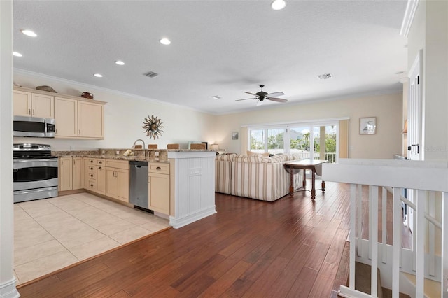 kitchen featuring appliances with stainless steel finishes, crown molding, a ceiling fan, cream cabinetry, and light wood-type flooring