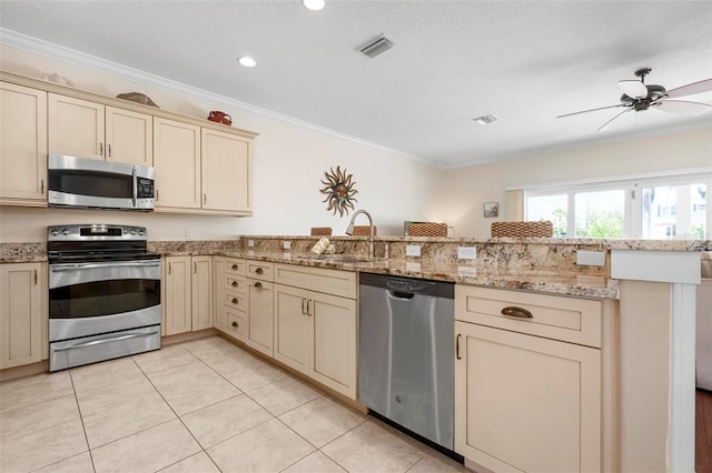 kitchen with stainless steel appliances, cream cabinets, a sink, a peninsula, and crown molding