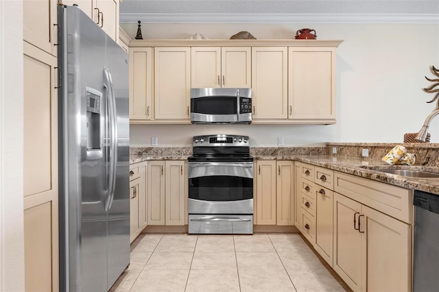 kitchen with appliances with stainless steel finishes, cream cabinetry, a sink, crown molding, and light stone counters