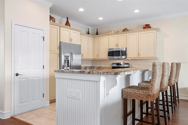 kitchen with stainless steel appliances, ornamental molding, a peninsula, cream cabinets, and a kitchen bar