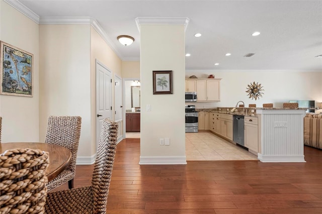 kitchen featuring stainless steel appliances, light wood-style flooring, a peninsula, ornamental molding, and open floor plan