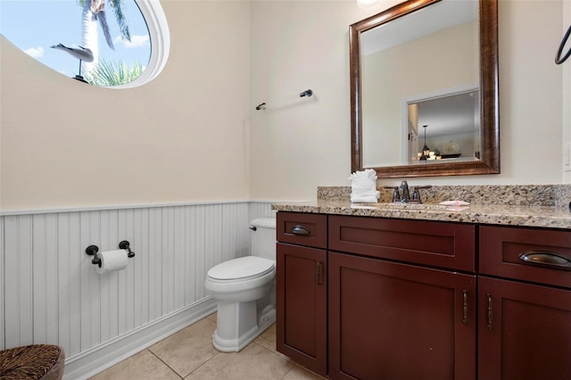 half bath featuring wainscoting, toilet, tile patterned flooring, and vanity