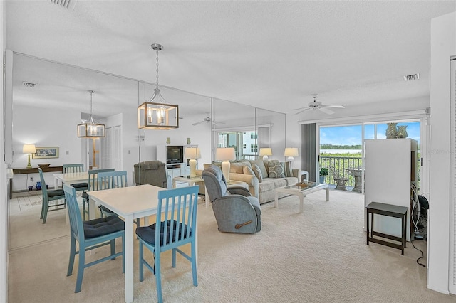 dining room featuring light carpet, a ceiling fan, a chandelier, and a textured ceiling