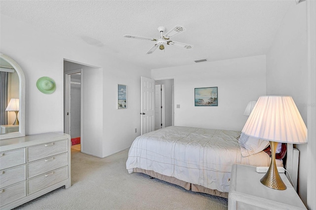bedroom with light colored carpet, a walk in closet, a textured ceiling, a ceiling fan, and a closet