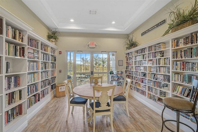 sitting room with wall of books, wood finished floors, a raised ceiling, recessed lighting, and baseboards