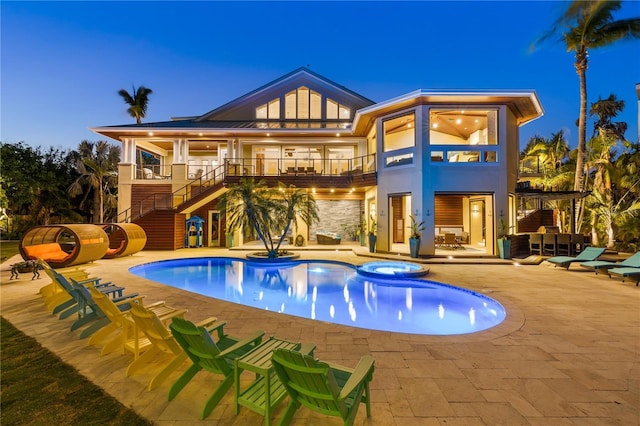 rear view of house featuring stairway, a balcony, a patio, a pool with connected hot tub, and stone siding