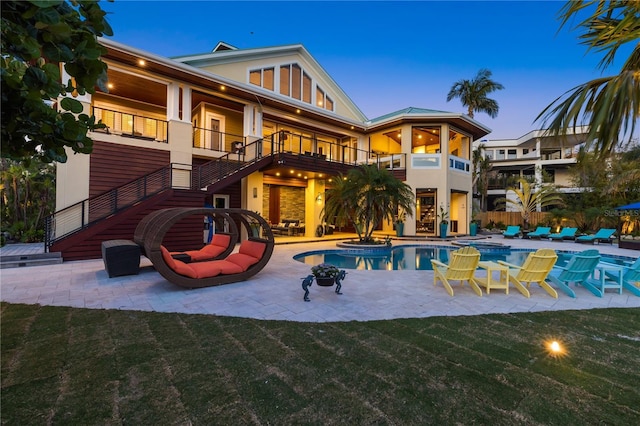 back of property at dusk with a balcony, a patio, stairs, stucco siding, and an outdoor pool