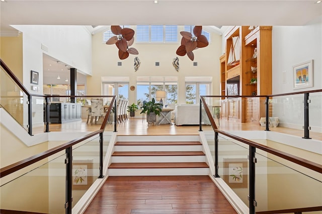 stairs featuring crown molding, wood-type flooring, ceiling fan, and a towering ceiling