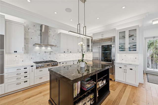 kitchen featuring wall chimney exhaust hood, stainless steel appliances, ornamental molding, tasteful backsplash, and glass insert cabinets