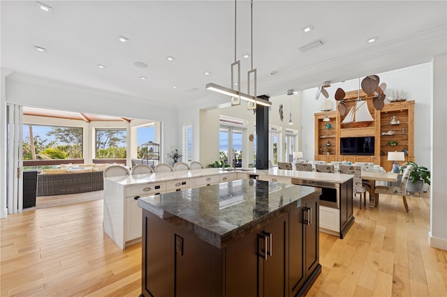 kitchen featuring a large island with sink, open floor plan, ornamental molding, light wood-style floors, and dark stone countertops