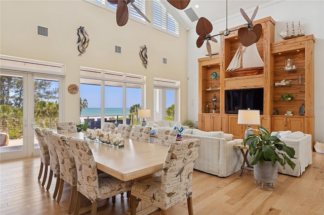 dining area with a high ceiling, light wood-style floors, ceiling fan, and french doors