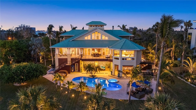 back of house with stairway, a standing seam roof, a pool with connected hot tub, metal roof, and a patio
