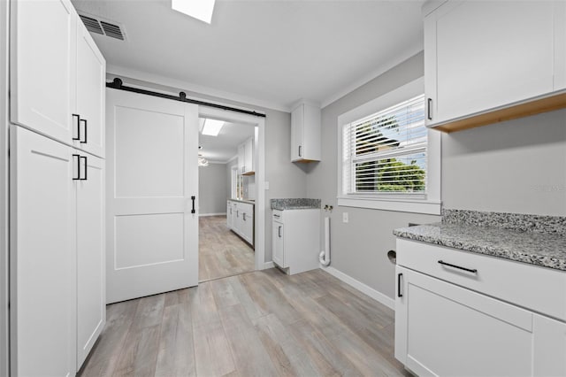 219 Vermont Ave, Saint Cloud, FL 34769 - kitchen featuring light wood-style flooring, a barn door, white cabinets, light stone counters, and baseboards