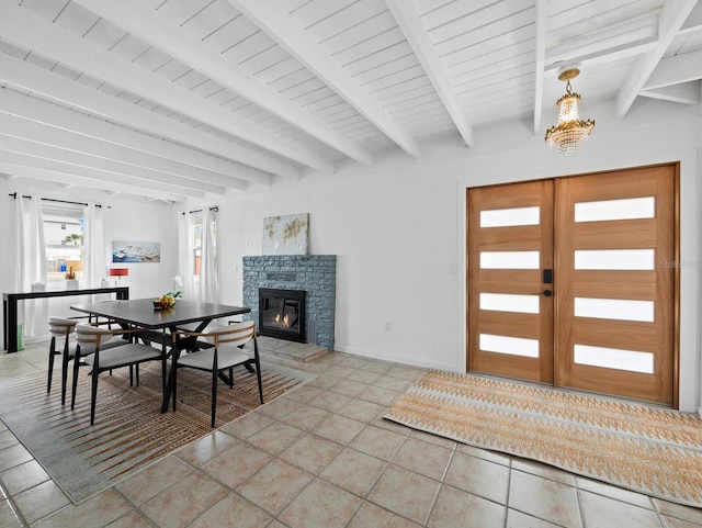 dining space with beam ceiling, a stone fireplace, light tile patterned floors, and baseboards