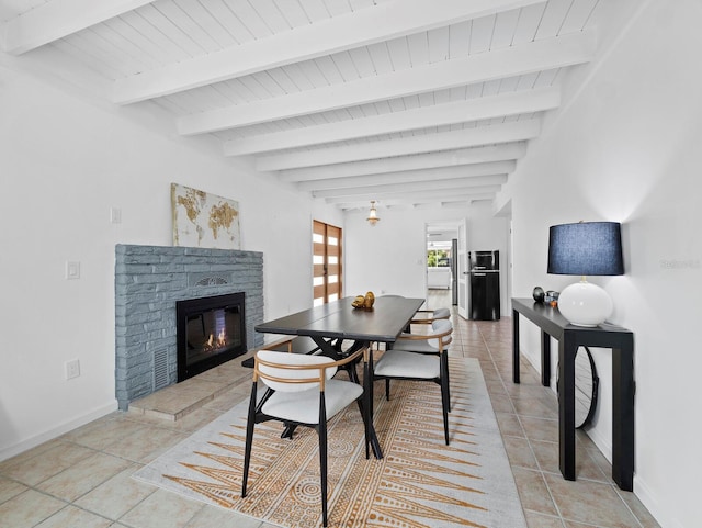 dining room with light tile patterned floors, a glass covered fireplace, wood ceiling, baseboards, and beam ceiling