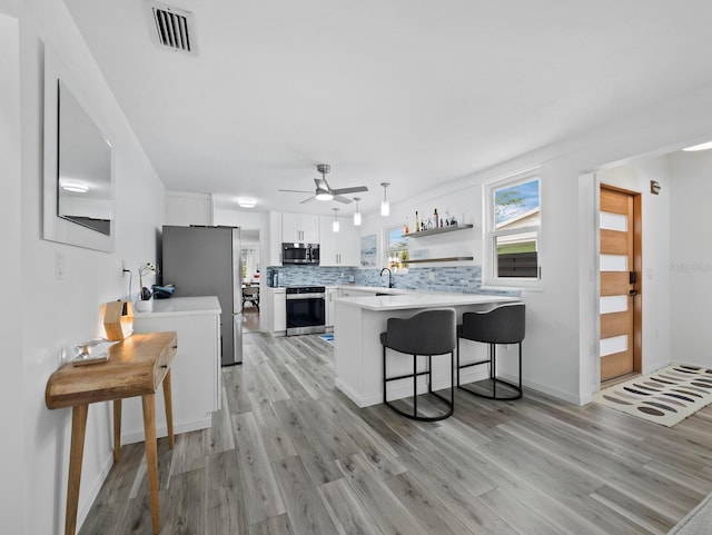 kitchen featuring stainless steel appliances, a peninsula, white cabinetry, a sink, and light wood finished floors