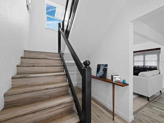 stairs with wood finished floors, baseboards, and a textured wall
