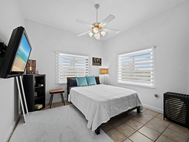 tiled bedroom featuring multiple windows, heating unit, baseboards, and ceiling fan