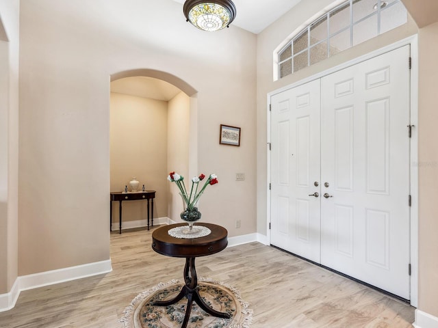 foyer entrance featuring arched walkways, light wood-type flooring, baseboards, and a high ceiling