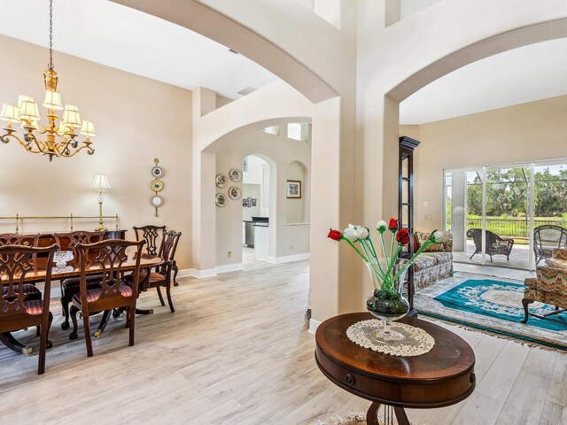 dining area with a chandelier, light wood-type flooring, arched walkways, baseboards, and a towering ceiling