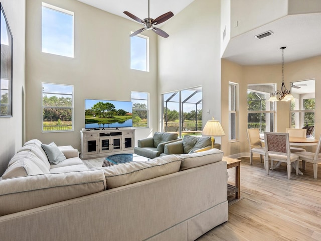 living room featuring a towering ceiling, light wood finished floors, ceiling fan, a chandelier, and healthy amount of natural light
