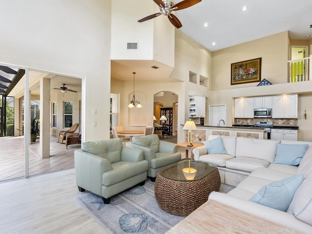 living room with ceiling fan, a high ceiling, arched walkways, light wood-type flooring, and recessed lighting