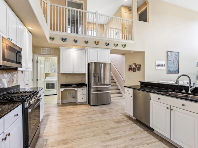 kitchen featuring appliances with stainless steel finishes, a towering ceiling, a sink, washer / dryer, and light wood-style floors