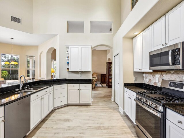 kitchen with appliances with stainless steel finishes, a high ceiling, arched walkways, a sink, and white cabinetry
