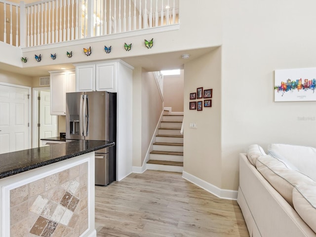 kitchen featuring stainless steel refrigerator with ice dispenser, a high ceiling, baseboards, open floor plan, and light wood-type flooring